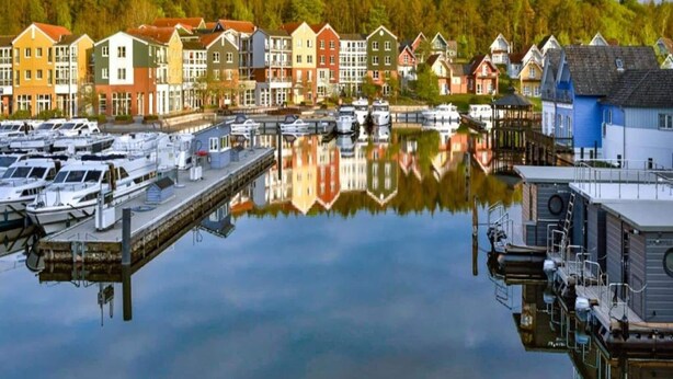 A marina with boats docked, a dock extending into calm water, and colorful buildings in the background.