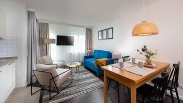 Ein modernes Wohnzimmer mit einem blauen Sofa, einem Holzessttisch und einem an der Wand befestigten Fernseher.