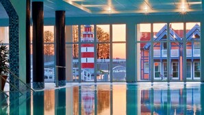 A swimming pool with clear reflections, large windows, and a view of a red and white lighthouse.