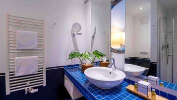 A modern bathroom with a large mirror, two sinks, a towel rack, and a shower area.