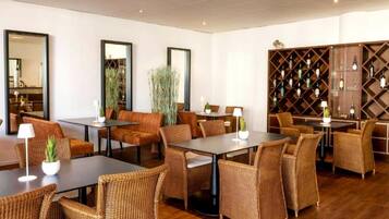 Un hall d’hôtel moderne, doté de meubles en osier, d’un présentoir à vin et de grands miroirs sur les murs.