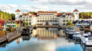 Un hotel frente a un canal, con un edificio central, barcos amarrados a lo largo del agua y casas coloridas a ambos lados.