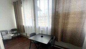 Una stanza con pavimento in legno, un tavolo con quattro sedie, un piccolo divano e una finestra con tende leggere.