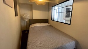 Una camera da letto piccola e ordinata con un letto singolo, una lampada a sospensione, una finestra con vista e un quadro appeso al muro.