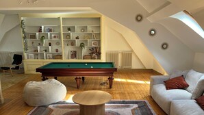 A cozy living room with a pool table, a sofa, and a bookshelf.