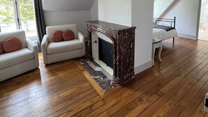 A spacious living room with a fireplace, wooden flooring, and a chandelier.