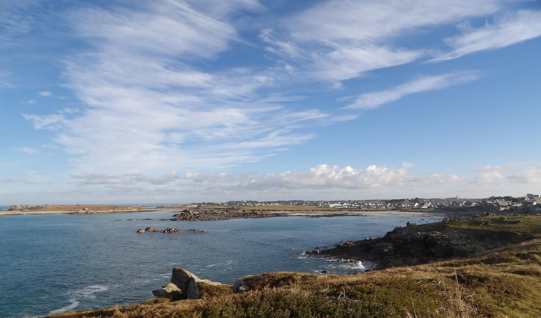 Un paysage côtier avec un ciel dégagé, une côte rocheuse et une ville située au loin.