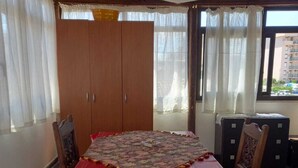 Ein Zimmer mit Holzboden, einem Tisch mit roter Tischdecke und Blick durch ein Fenster.