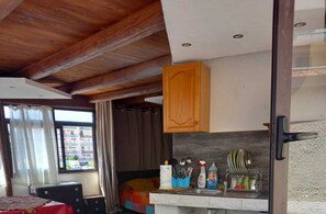 Una habitación con techo de madera, un área de cocina con un lavamanos, armarios y diversos utensilios de cocina.
