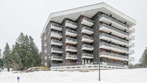 Ein mehrstöckiges Gebäude mit Balkonen, einem Parkschild und verschneiter Umgebung.