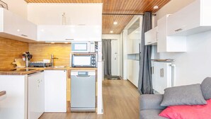 Eine kleine Küche mit Mikrowelle, Toaster und Geschirrspüler, ein graues Sofa mit einem roten Kissen und eine Holzbalkendecke.
