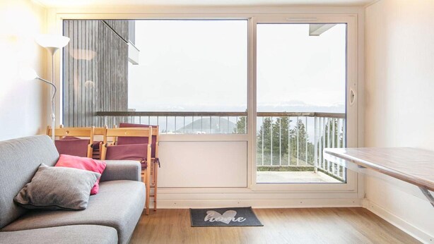 Ein Zimmer mit grauem Sofa, einem Holztisch, einer Bank und einem großen Fenster mit Bergblick.
