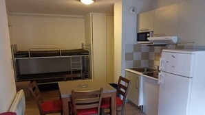 Ett kompakt kök med ett matbord, stolar, en mikrovågsugn, ett kylskåp och en våningssäng.