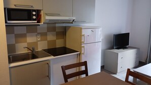 Ett kompakt kök med mikrovågsugn, spis, diskho, kylskåp och en liten tv placerad på ett skåp.