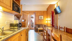 A kitchen with wooden cabinets, a microwave, and a coffee maker. There is a dining area with a wooden table and chairs. A television is mounted on the wall. - Pet-Friendly Family Home with Balcony (Saint-Sorlin-d´Arves)