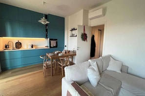 Eine moderne Küche mit türkisfarbenen Schränken, einem Esstisch und einem beigen Sofa in einem Wohnbereich.