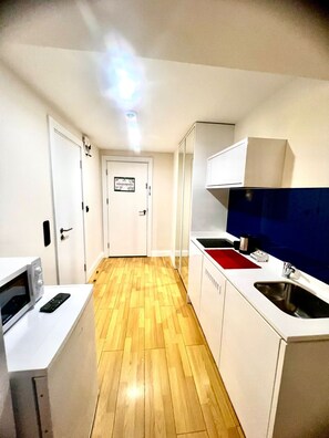 Un pasillo estrecho que da a una cocina con microondas, lavamanos y armarios.