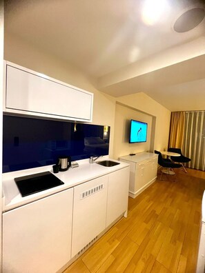 A modern kitchen with a built-in stove, a sink, and a flat-screen TV mounted on the wall. - Modern Sea-View Studio in Orbi City Batumi | Steps from the Beach (Batumi)