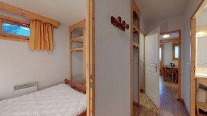 A bedroom with a bed, a window with curtains, a wooden headboard, and a wooden door leading to a bathroom. - Apartment in Chamrousse Near Cable Car (Chamrousse)