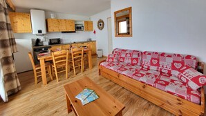 A compact living space with a kitchenette, wooden furniture, and a patterned sofa. - Apartment in Chamrousse Near Cable Car (Chamrousse)