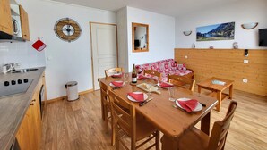 A compact kitchen with a sink, stove, and wooden cabinets. A dining table with chairs is set for two, and a wooden bench with cushions is against the wall. - Apartment in Chamrousse Near Cable Car (Chamrousse)