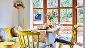 A cozy room with a yellow sofa, a wooden table with breakfast items, and a large window with a view of greenery. - Sea Gables (Exmouth)