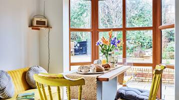 A cozy room with a yellow sofa, a wooden table with breakfast items, and a large window with a view of greenery.