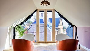 A room with a sloped ceiling, two orange chairs, a blue rug, and a view of a brick building through a glass door. - Sea Gables (Exmouth)