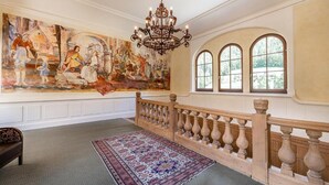A grand room with a large mural, a chandelier, and a wooden railing. - Naturhotel Schloss Kassegg (Sankt Gallen)
