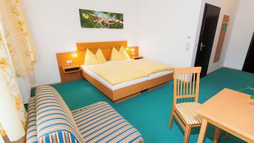 A hotel room with a bed, a wooden table, a chair, a bench, and a wall-mounted picture.