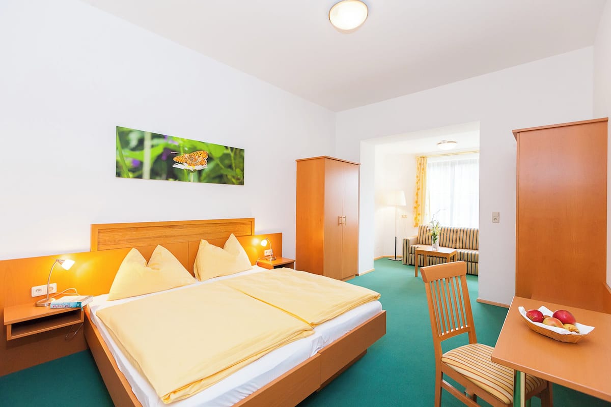 A hotel room with a bed, bedside table, lamp, and a dining area with a table and chairs.