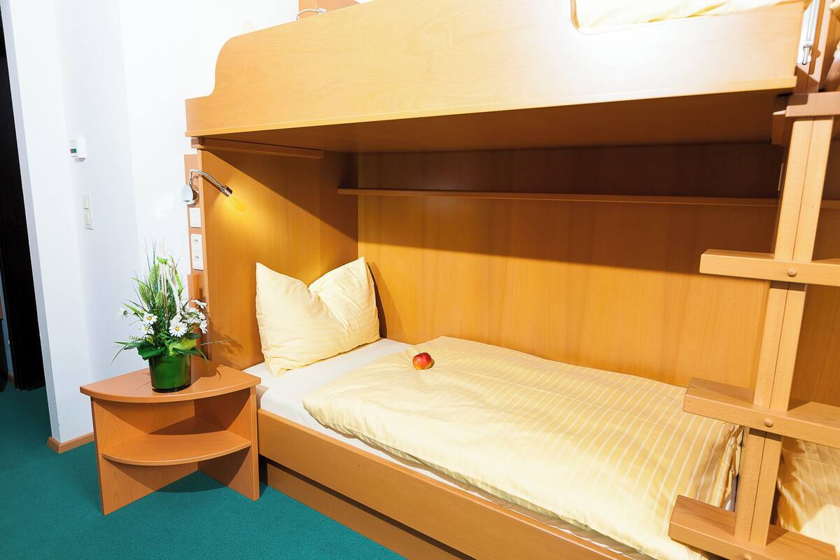 A bunk bed with a wooden headboard, a bedside table with a potted plant, and a single apple on the bed.