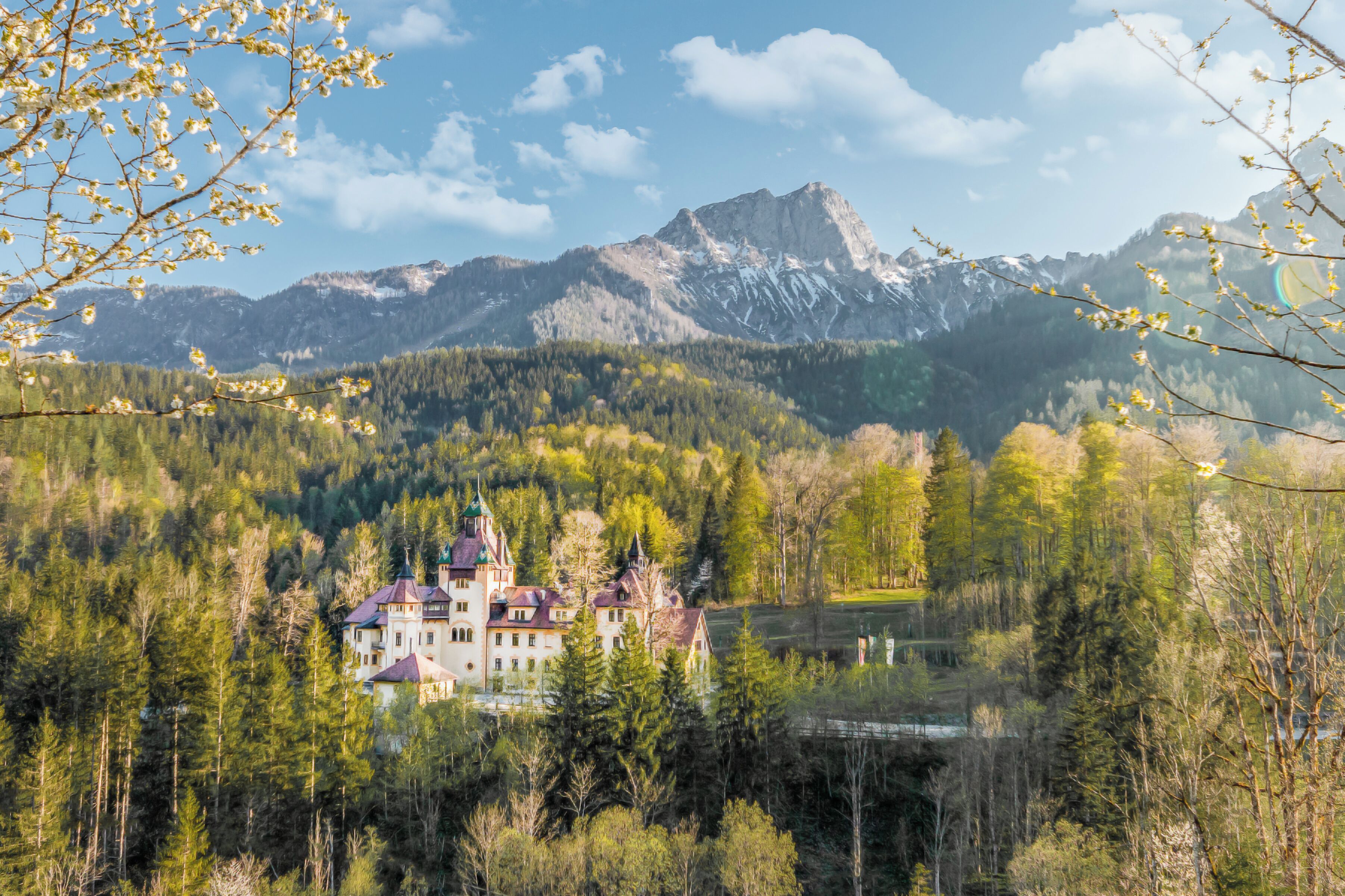A large, historic building surrounded by dense forest and mountains.