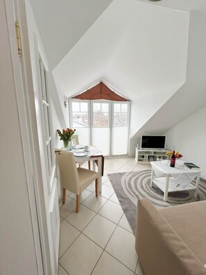 A modern loft apartment with a dining area, a living room with a TV, and a large window with a red awning. - Haus Baylan - Welcome to Haus Baylan, a charming vacation home in (Sylt)
