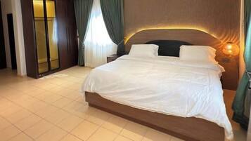 A large bed with a wooden headboard, a bedside lamp, and a view of a room with a wardrobe and curtains.