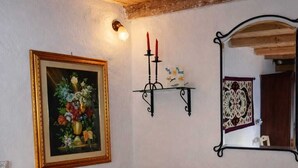 A cozy room with a wooden ceiling, a framed floral painting, a candle holder, a patterned cushion, and a mirror. - Laura's Little Houses: Mondello 1 (Palermo)