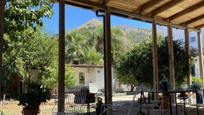 A covered outdoor seating area with tables and chairs, surrounded by trees and a mountain view. - Laura's Little Houses: Mondello 1 (Palermo)