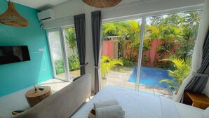 A bedroom with a large bed, a TV mounted on the wall, and a view of a swimming pool and garden. - Canggu 1 BR Private Pool Villa Polly (Canggu)