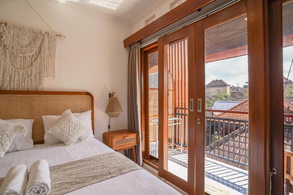Habitación de hotel con una cama grande, un tapiz de macramé y un balcón con vistas al vecindario.