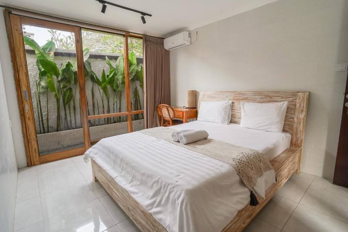 Un dormitorio con una cama grande, un cabecero de madera, una silla y vistas a un jardín a través de un ventanal corredero.