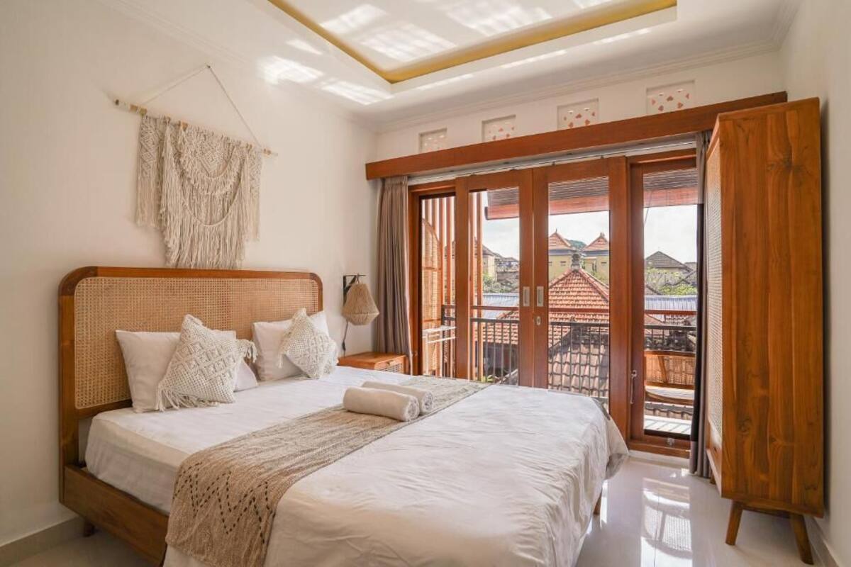 Un dormitorio con una cama grande, cabecera de madera y vistas a un balcón con mobiliario exterior.