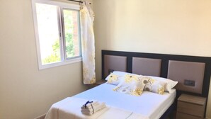 A neatly made bed with a white bedspread and matching pillows, a small bedside table, and a window with curtains. - Elegant house w/pool | Aroa by HL (barcelona)
