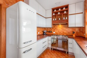 Una cucina con mobili bianchi, un frigorifero bianco, un fornello e una mensola di legno con utensili da cucina.