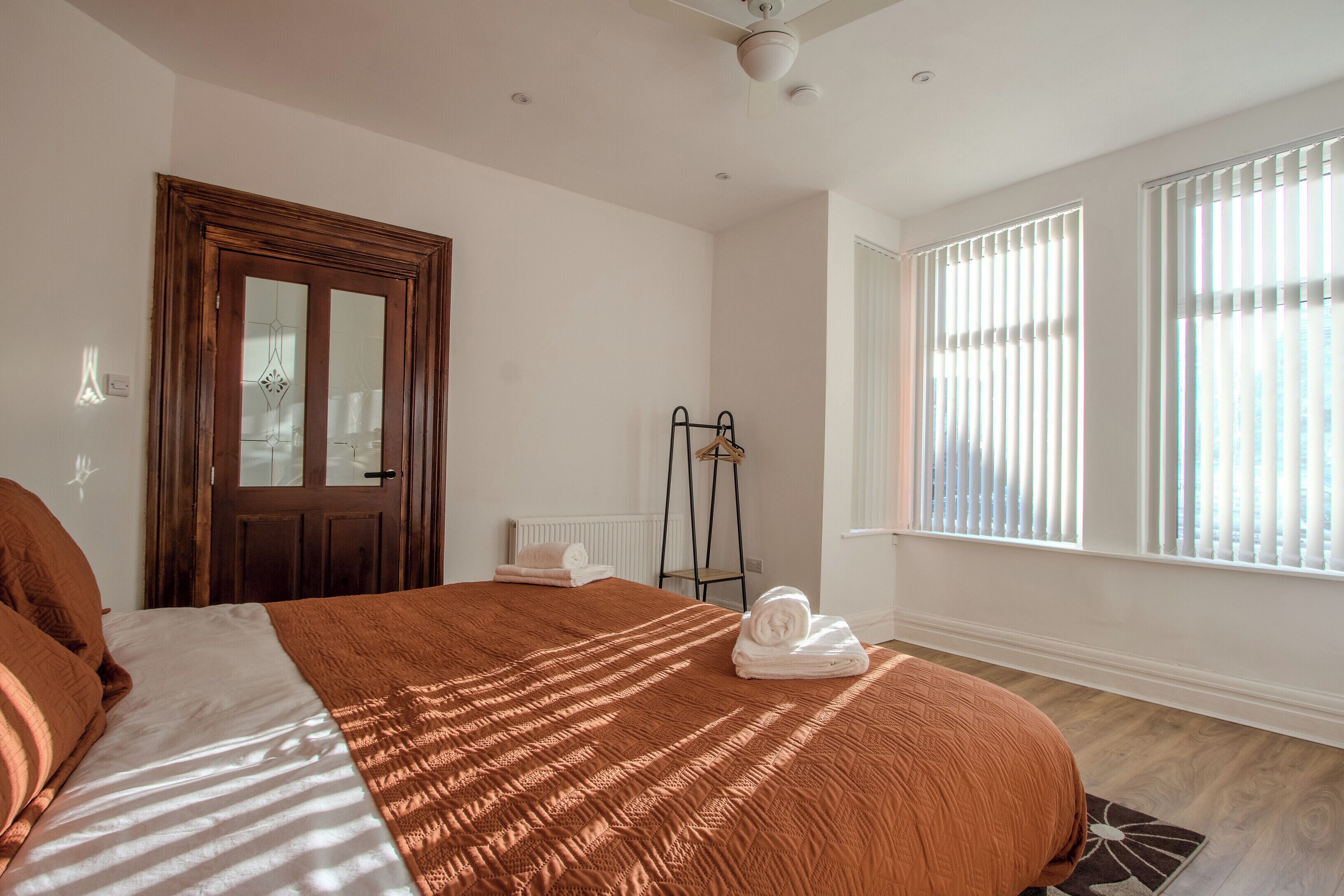 Een slaapkamer met een groot bed, een houten deur, een radiator en een raam met jaloezieën.