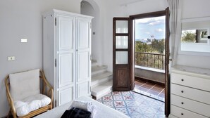 A bedroom with a bed, a wardrobe, a chair, and a balcony with a view. - Apartment with beautiful sea and mountain views. (santa maria navarrese)