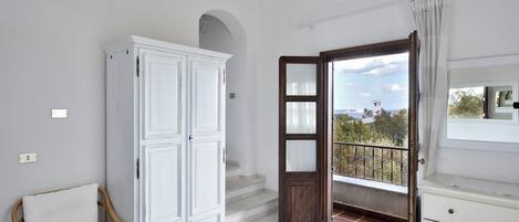 Ein Schlafzimmer mit Bett, Kleiderschrank, Stuhl und einem Balkon mit Blick.