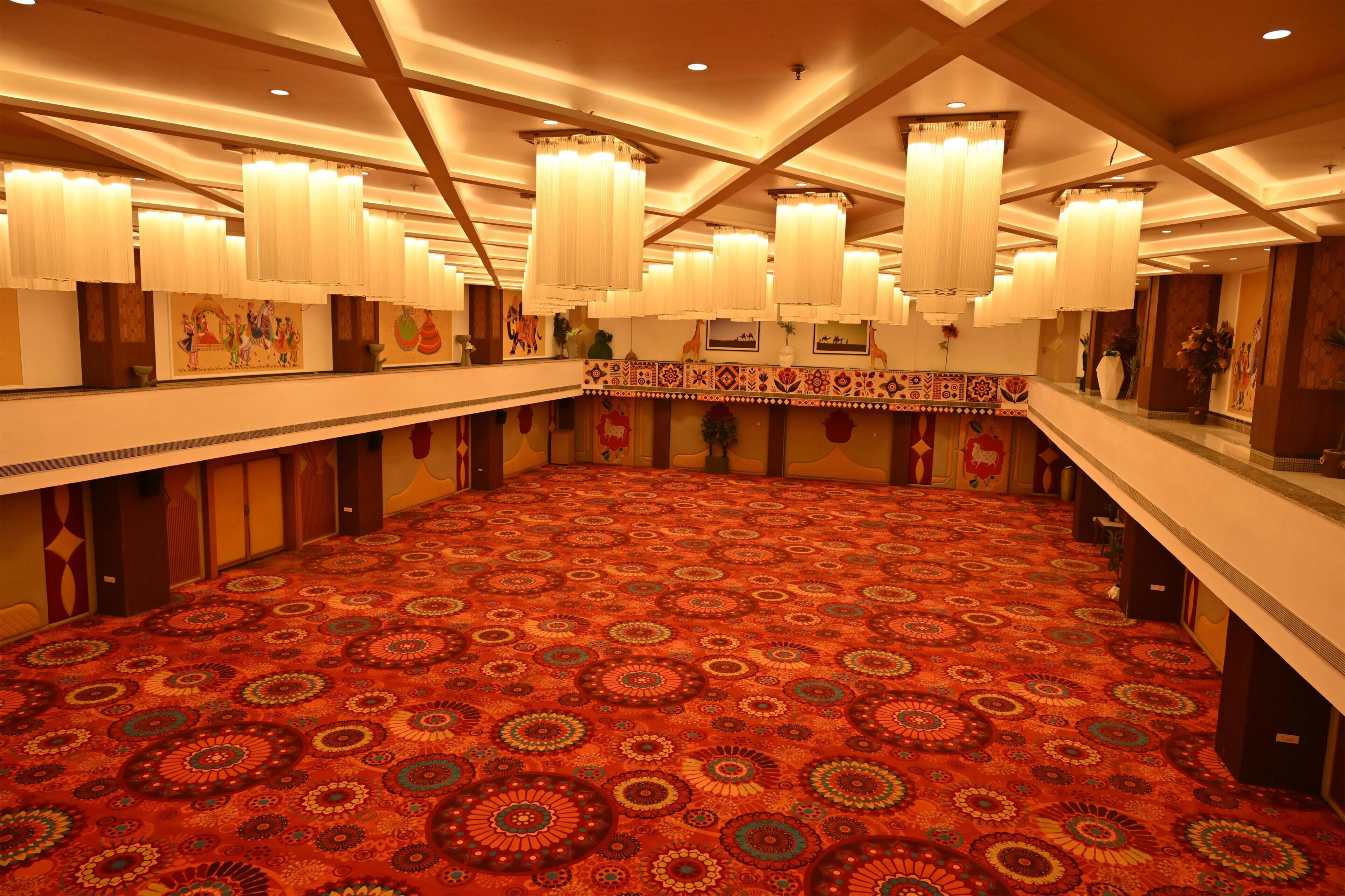 A spacious hall with patterned carpet, multiple chandeliers, and artwork on the walls.