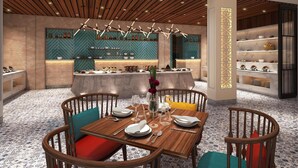 Un'area pranzo moderna con un tavolo centrale apparecchiato per un pasto, circondato da sedie di legno con cuscini colorati.