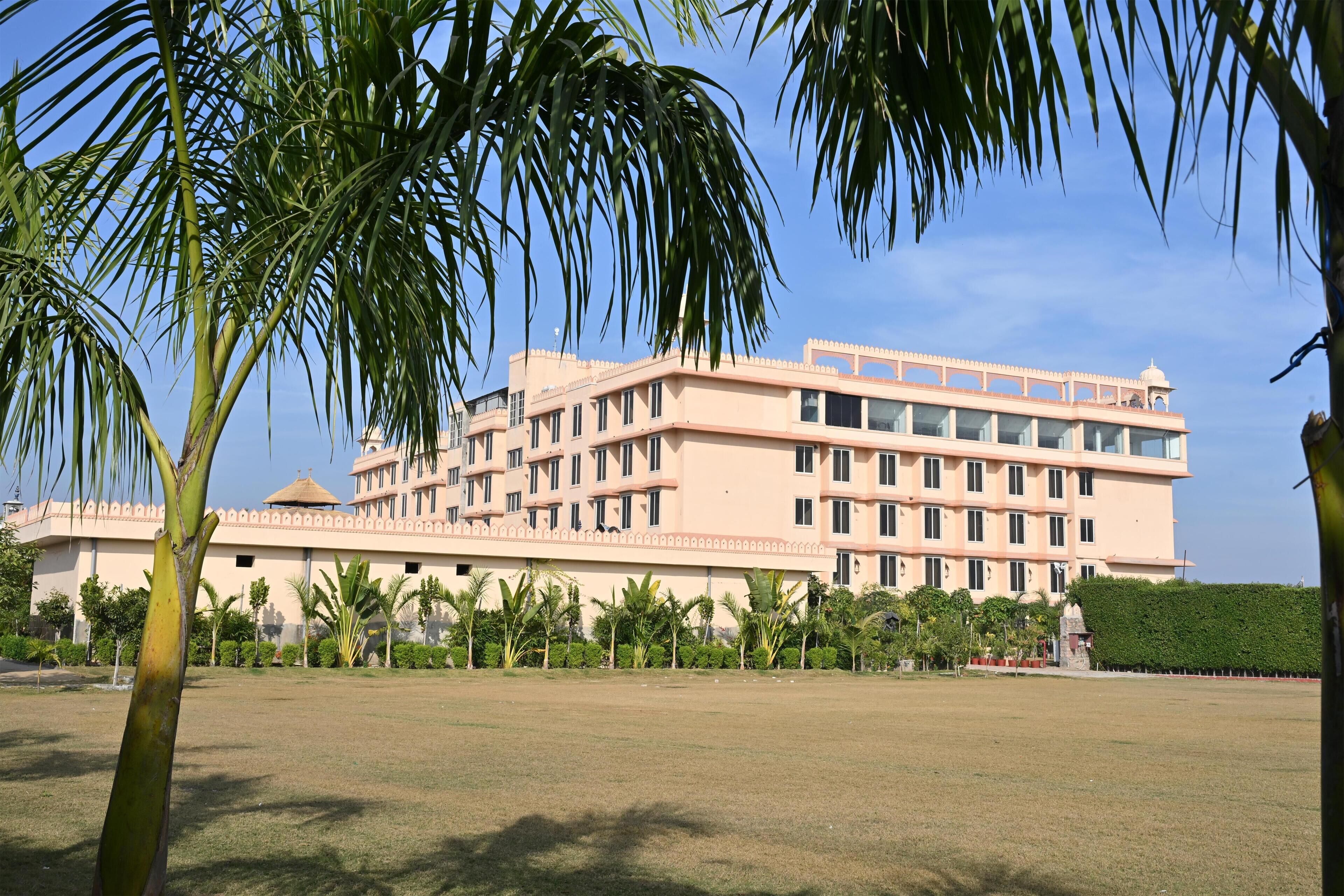 A multi-story building with a flat roof, surrounded by a well-maintained lawn and palm trees.