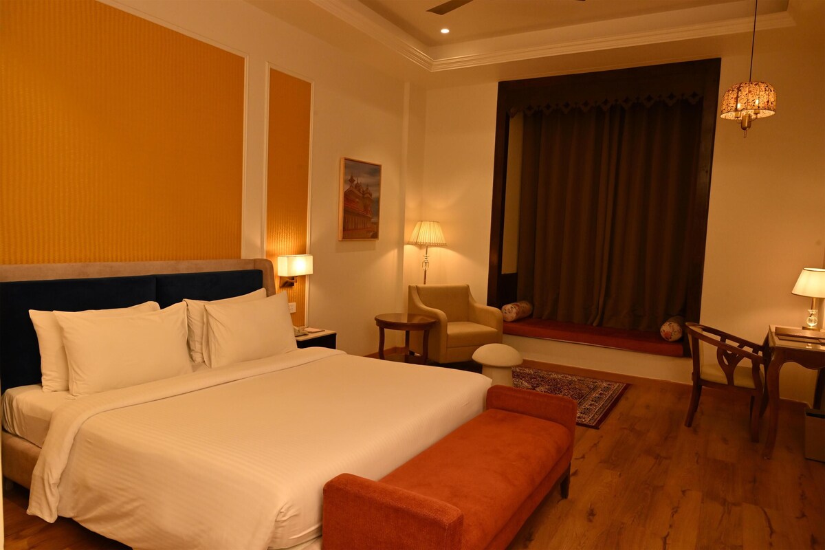 Ein Hotelzimmer mit einem großen Bett, einer Couch, einem Sessel, einem kleinen Tisch, einer Lampe, einem Gemälde und einem fenster mit Vorhängen.